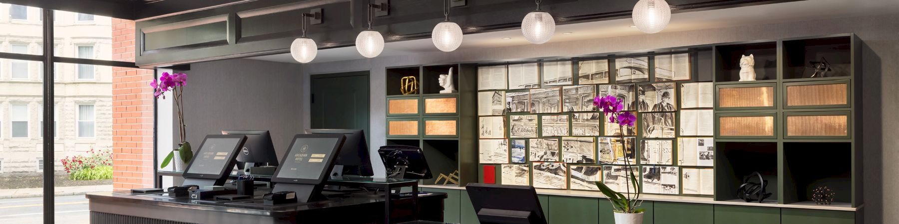 A modern reception area with dark wood desks, computer terminals, green storage cabinets, and a wall of notes/artwork; bright flowers add color.