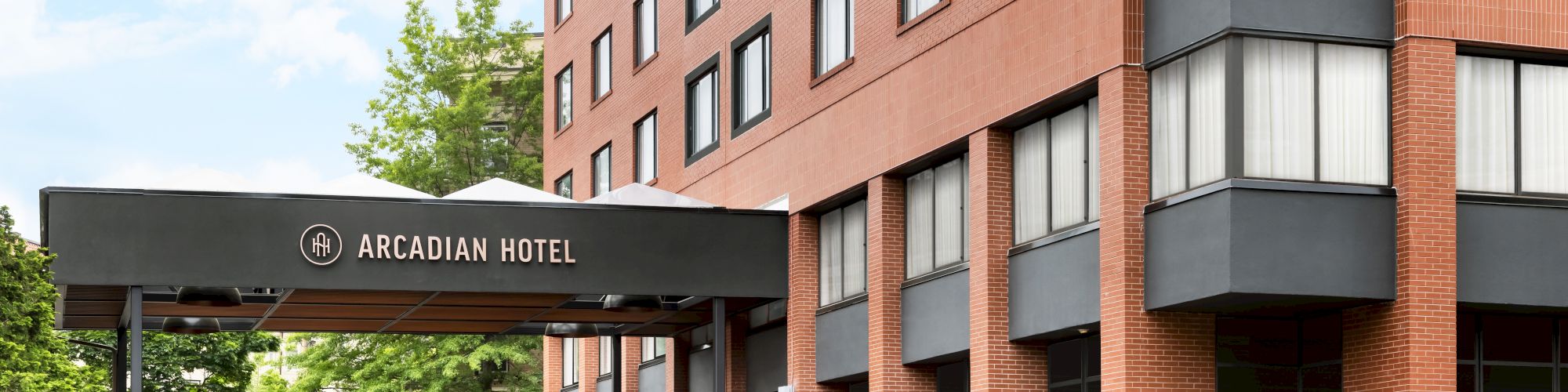 The Arcadian Hotel sign is on the entrance of a multi-story brick building with windows under a blue sky.