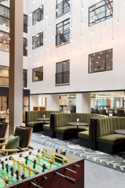 A modern hotel lobby with a foosball table, cozy green couches, glass walls, and a bright open-air feel, inviting guests to relax and socialize.