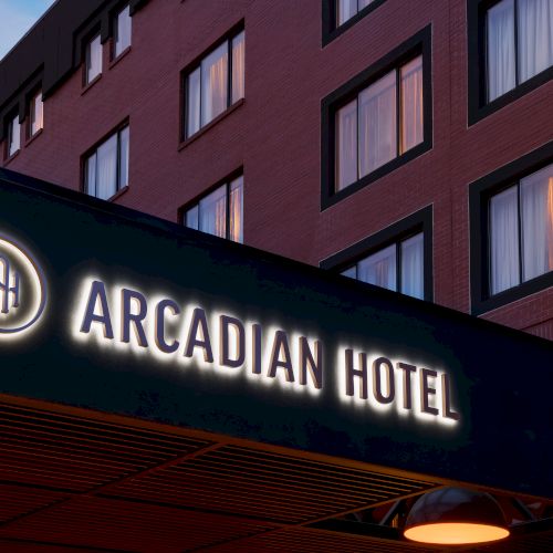 A hotel exterior sign reading &ldquo;Arcadian Hotel&rdquo; with warm windows on a brick building at dusk.