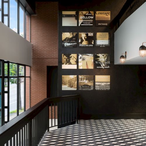 A modern hallway with brick walls, framed book-cover posters, a checkered floor, and wall lamps by large windows, .