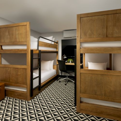 A stylish hotel room featuring two open wooden bunk beds, a desk, a chair, and a patterned carpet.
