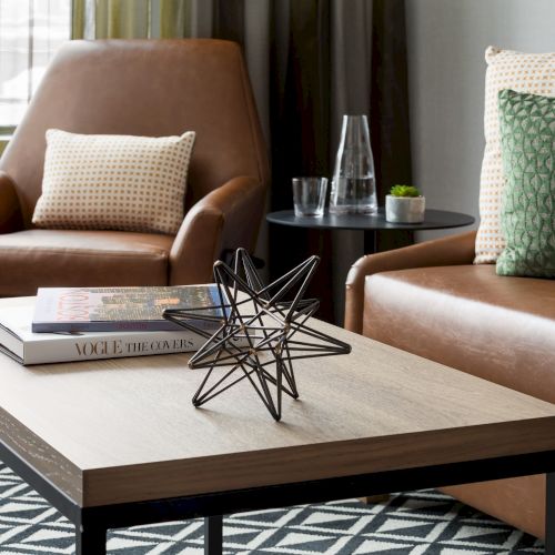 A cozy living room: leather armchair, patterned pillows, round side table with drinks, and a coffee table with books and a star.