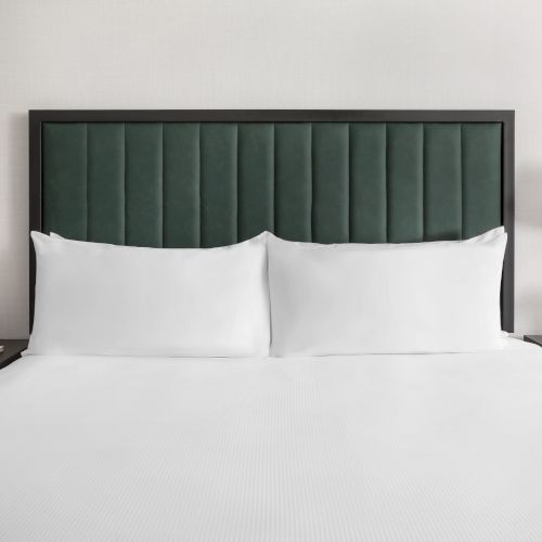 A modern hotel-style bedroom: white bed with green tufted headboard, two lamps, nightstands, and a vase of orange roses.