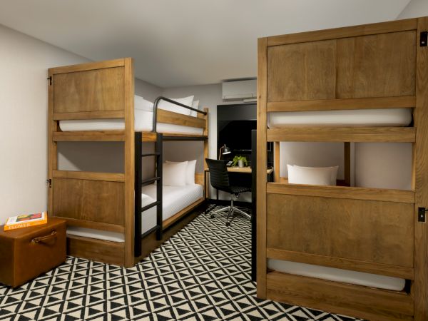 A room with two wooden bunk beds, a desk area, and a patterned floor, neatly arranged with neutral colors.