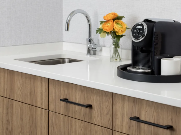 A modern kitchen counter with a sink, wooden cabinets, a coffee machine, a vase of orange flowers, and a couple of mugs on the side.