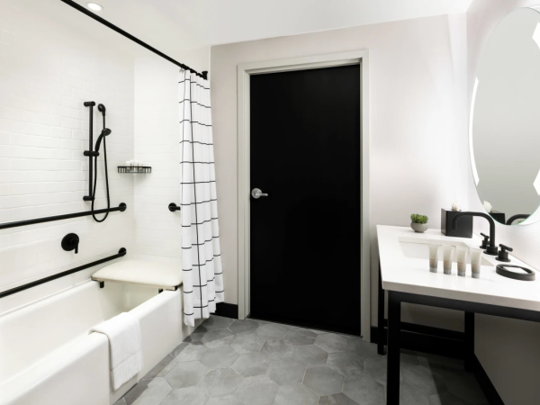 A modern accessible bathroom with a bathtub, walk-in shower, black fixtures, a large wall mirror, and a white sink vanity; stays tidy and bright.