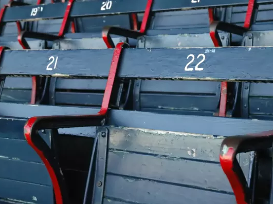 Seats in stadium: blue wooden benches with red arm supports and white numbers.