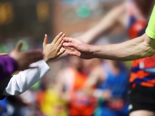 Kids and runners high-five as a cheering crowd forms a colorful backdrop, celebrating teamwork and athletic spirit.