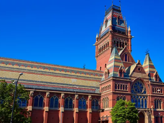 A red brick, ornate Gothic-style train station or courthouse with a tall, detailed clock tower, arched windows, and a bright blue sky.