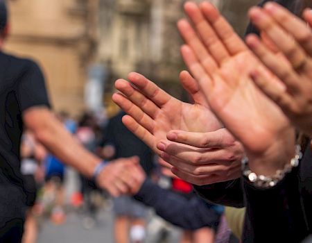 A line of people claps along a street, cheering as runners pass by, capturing a moment of support and celebration.