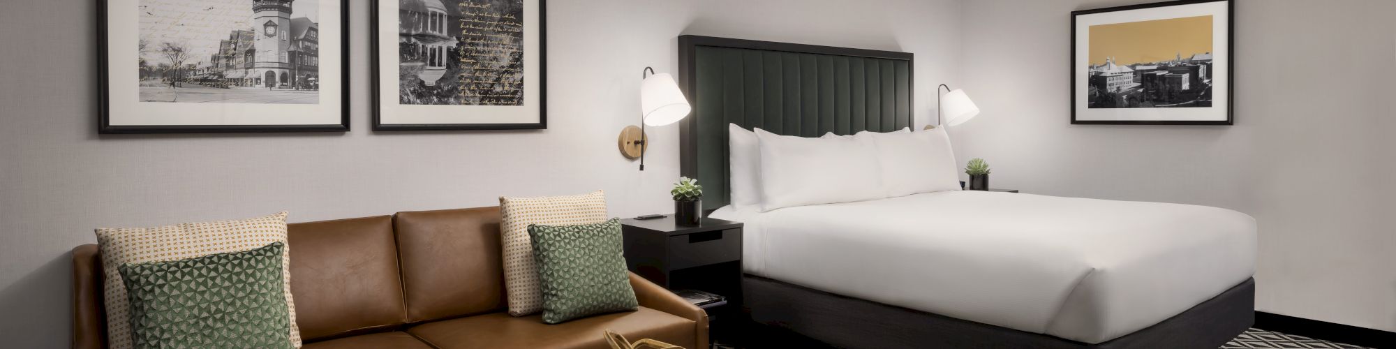 A hotel suite with a brown leather sofa, geometric carpet, coffee table, and a large bed with a dark headboard, framed wall art, and bedside lamps.