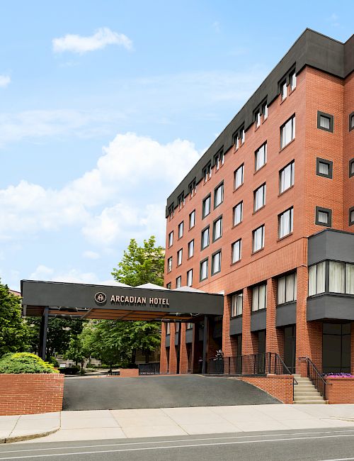 A red-brick hotel building with a sign reading Arcadian Hotel, surrounded by trees under a blue sky.