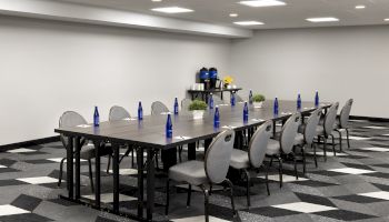 A conference room with a long boardroom table set with blue bottles, cups, plants, and gray chairs.