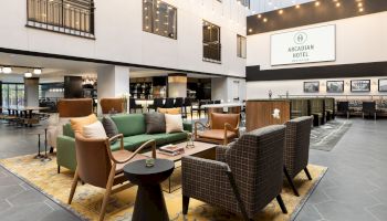 A cozy hotel lobby with lounge seating, string lights, and an &ldquo;Arcadian Hotel Brookline&rdquo; sign.