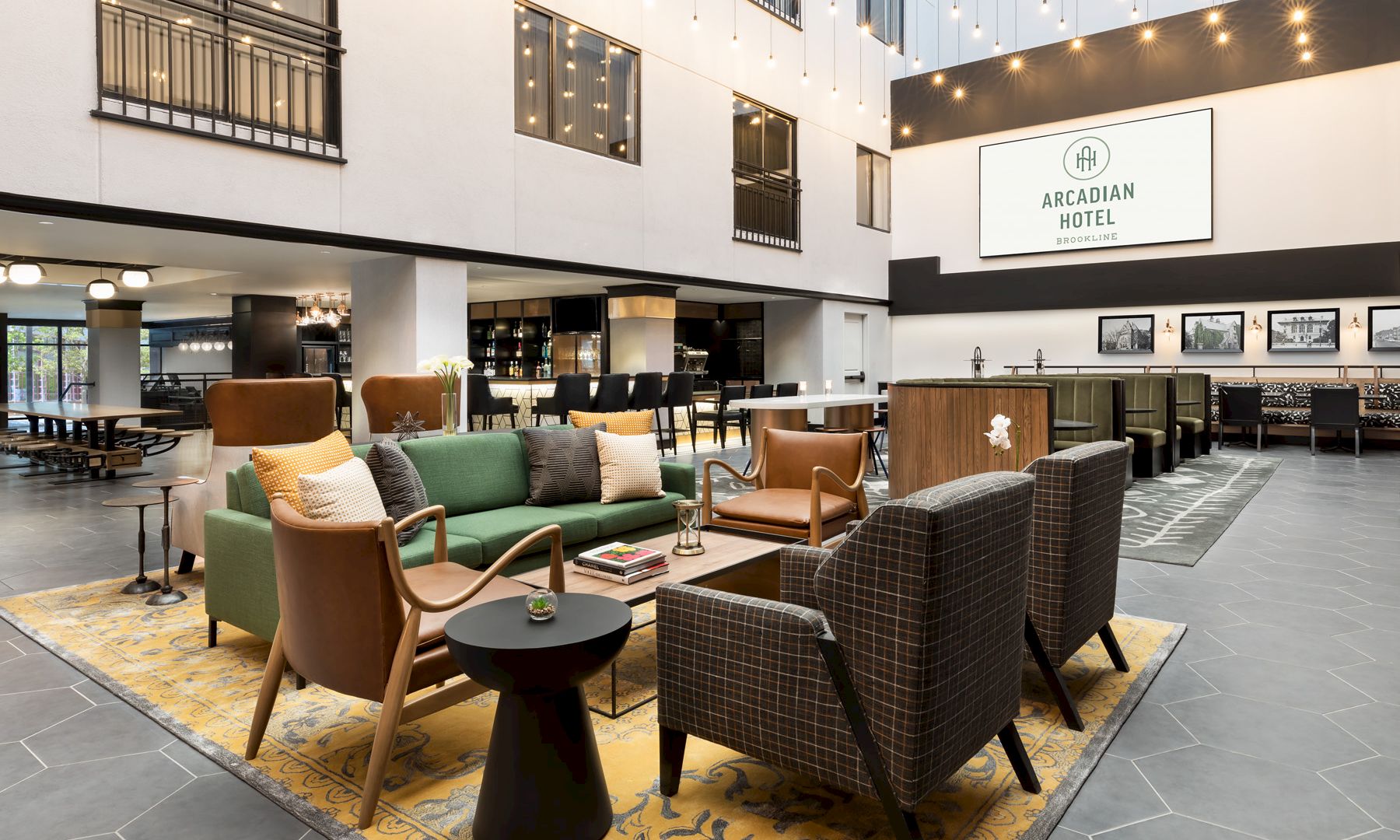 A modern hotel lobby lounge at the Arcadian Hotel, with sofas, chairs, warm string lights, and a reception bar.