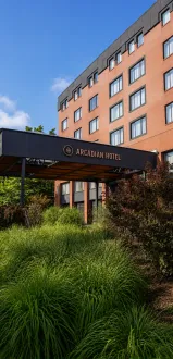 A brick hotel building with an outdoor awning marked “Arcadian Hotel” under a bright blue sky.
