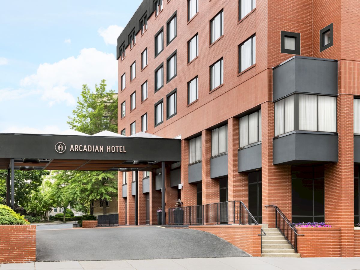 A brick hotel building labeled Arcadian Hotel with windows, awnings, and steps under a bright sky.