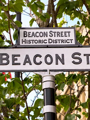 A street sign reads “BEACON ST.” beneath “Beacon Street Historic District,” framed by leafy green trees.