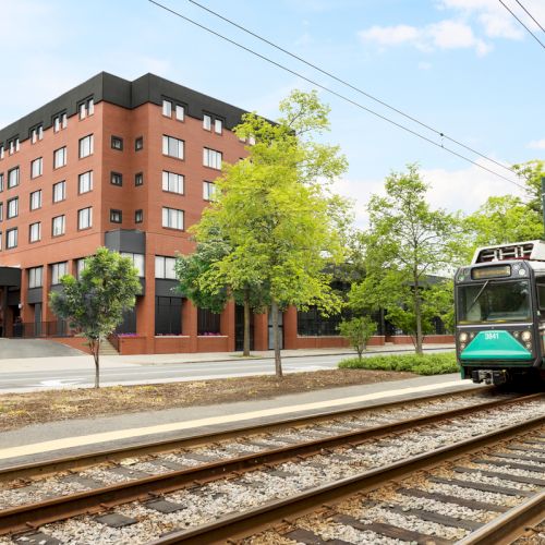 A red-brick Arcadian Hotel beside railway tracks as a green-and-white tram approaches through leafy trees.