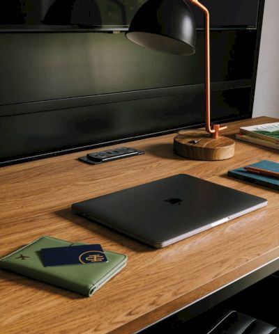 A desk setup: a black lamp with a copper stand, a laptop, a phone, a notebook, and books by a window.