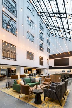 A modern hotel atrium with cozy lounge seating, warm string lights, and large windows in a glass-roof courtyard ending.