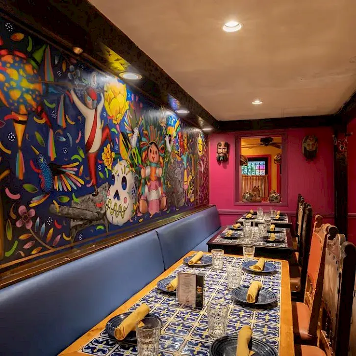 A brightly mural-covered restaurant booth with blue-and-white tablecloths, glasses, and candles, set for a meal.