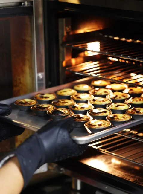 A gloved hand puts a tray of golden pastries in a hot oven.
