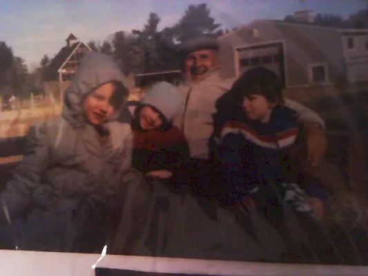 A blurry outdoor winter photo of three people in warm jackets posing in a driveway with houses in the background.