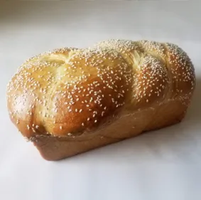 A braided loaf of bread, sprinkled with sesame seeds, on a light background, fresh and golden.